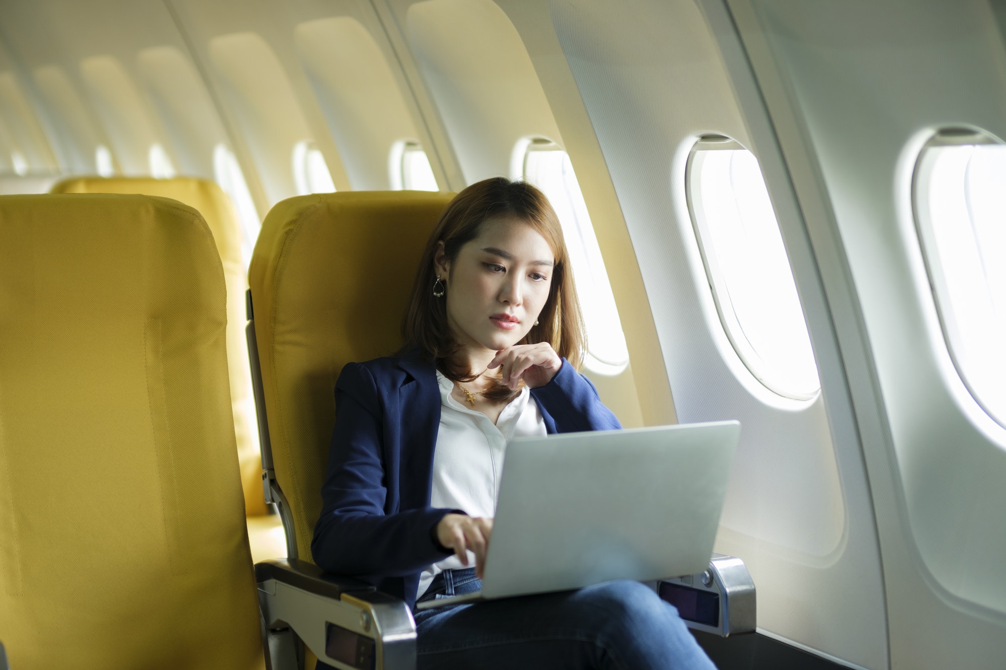 Business woman working on laptop while sitting in airplane.