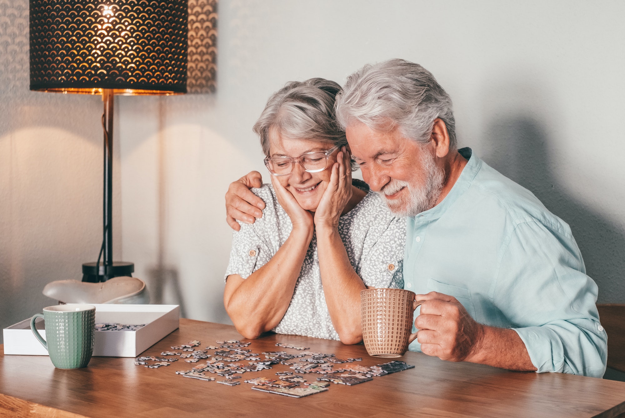 Carefree senior couple at home spend time together doing a puzzle on the wooden table